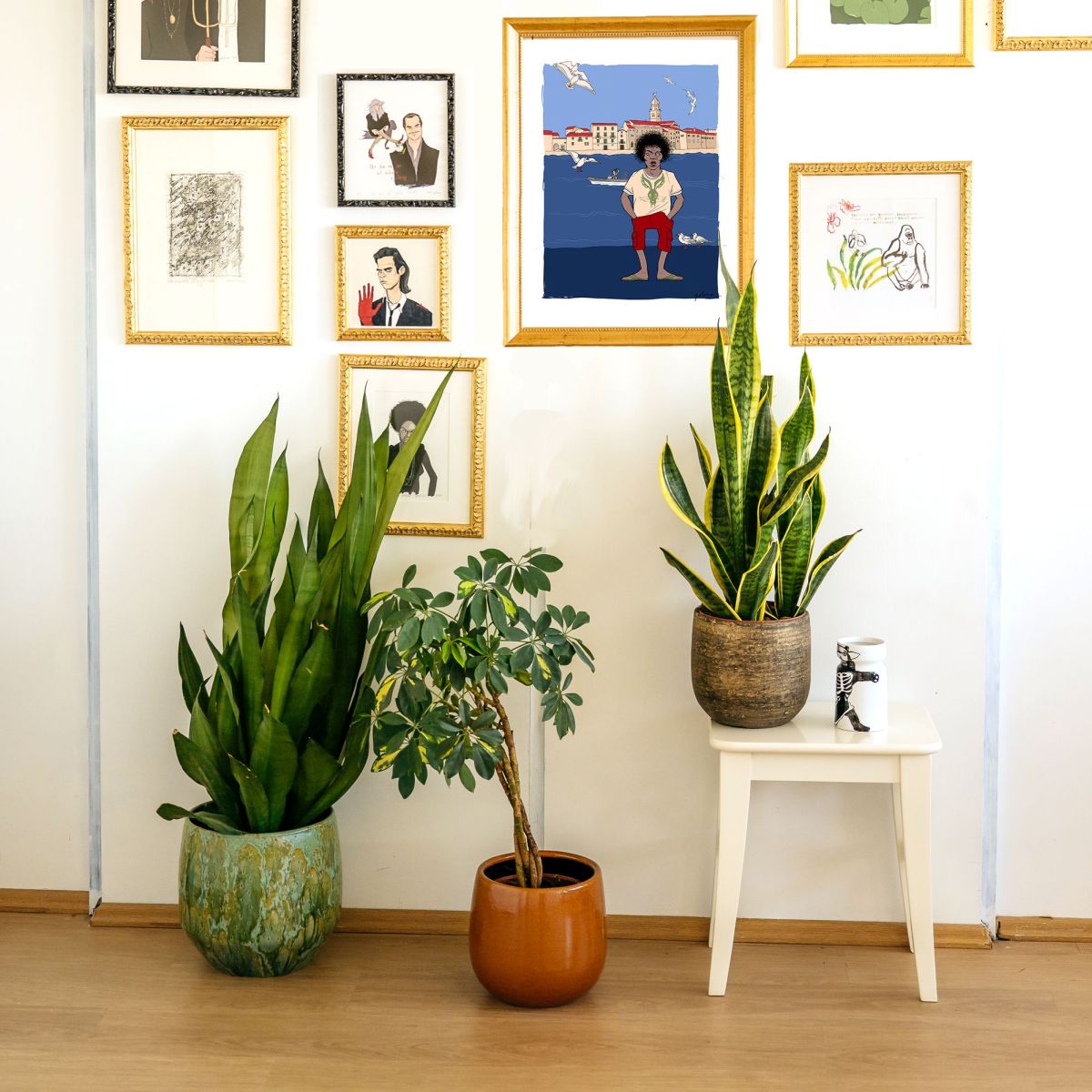 Room interior with framed artworks on the wall and potted plants on the floor.
