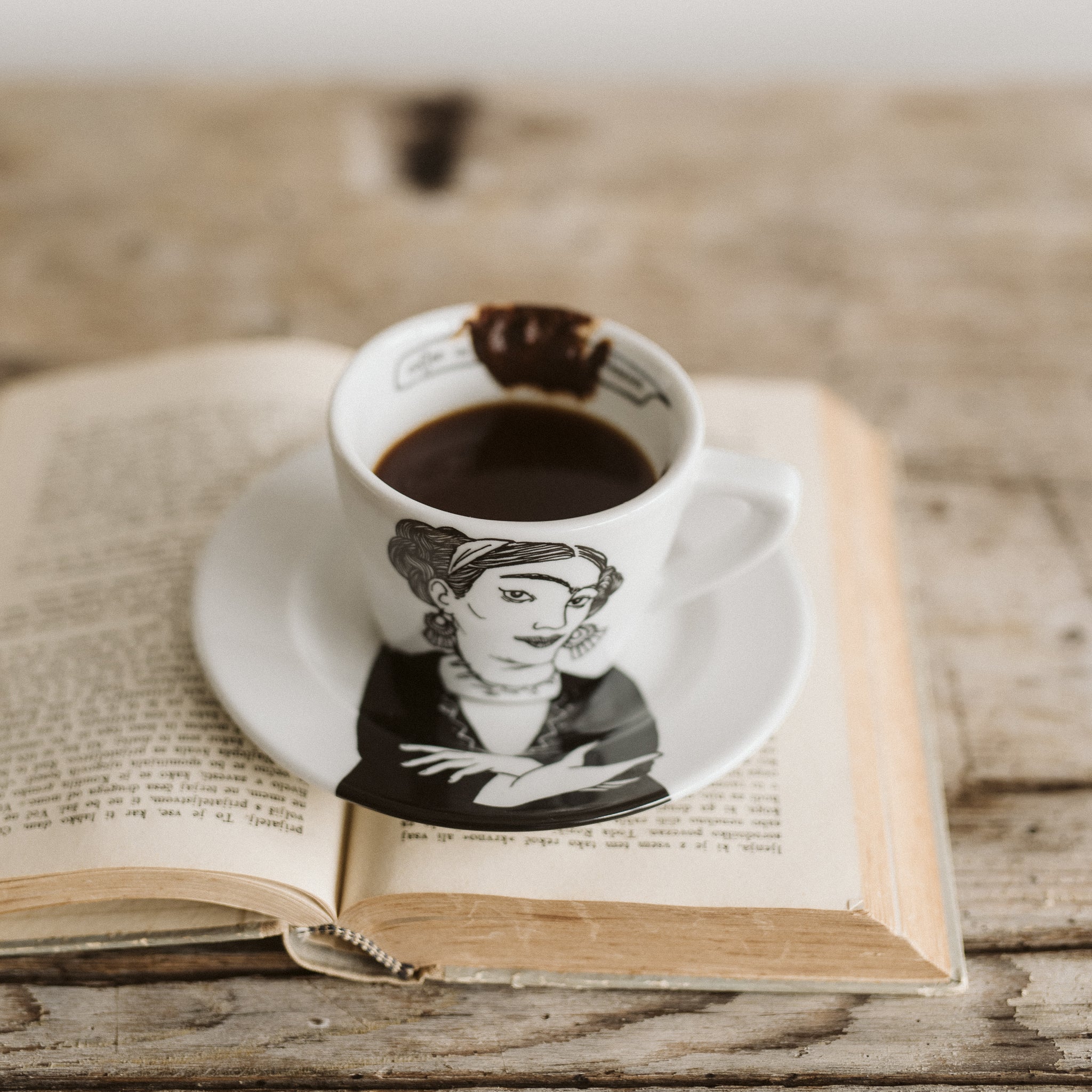 Polonapolona FRIDA 180ml porcelain white cappuccino set of cup and saucer resting on a book